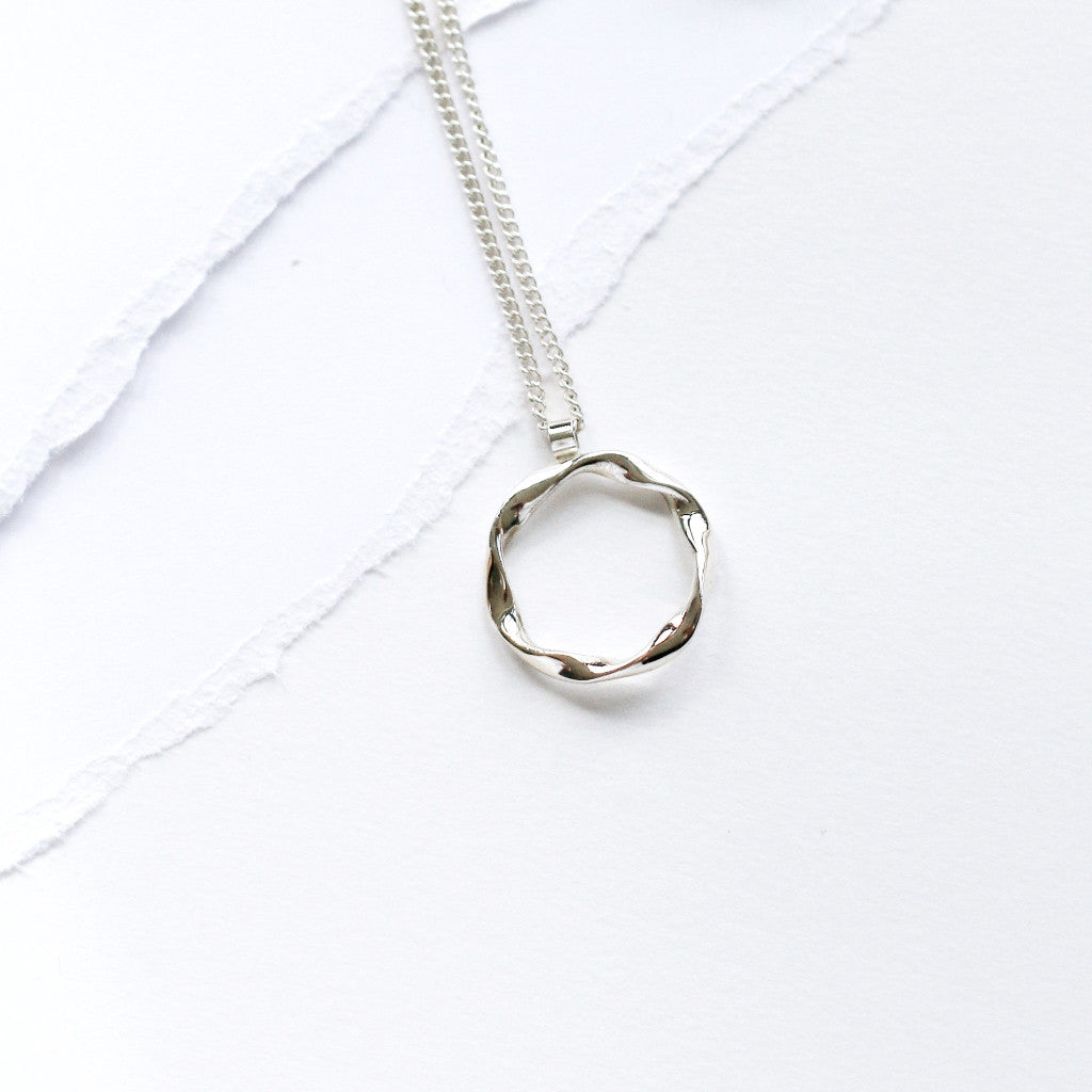 A silver pendant necklace with a twisted circle design on an 18-inch curb chain, displayed on a white background.