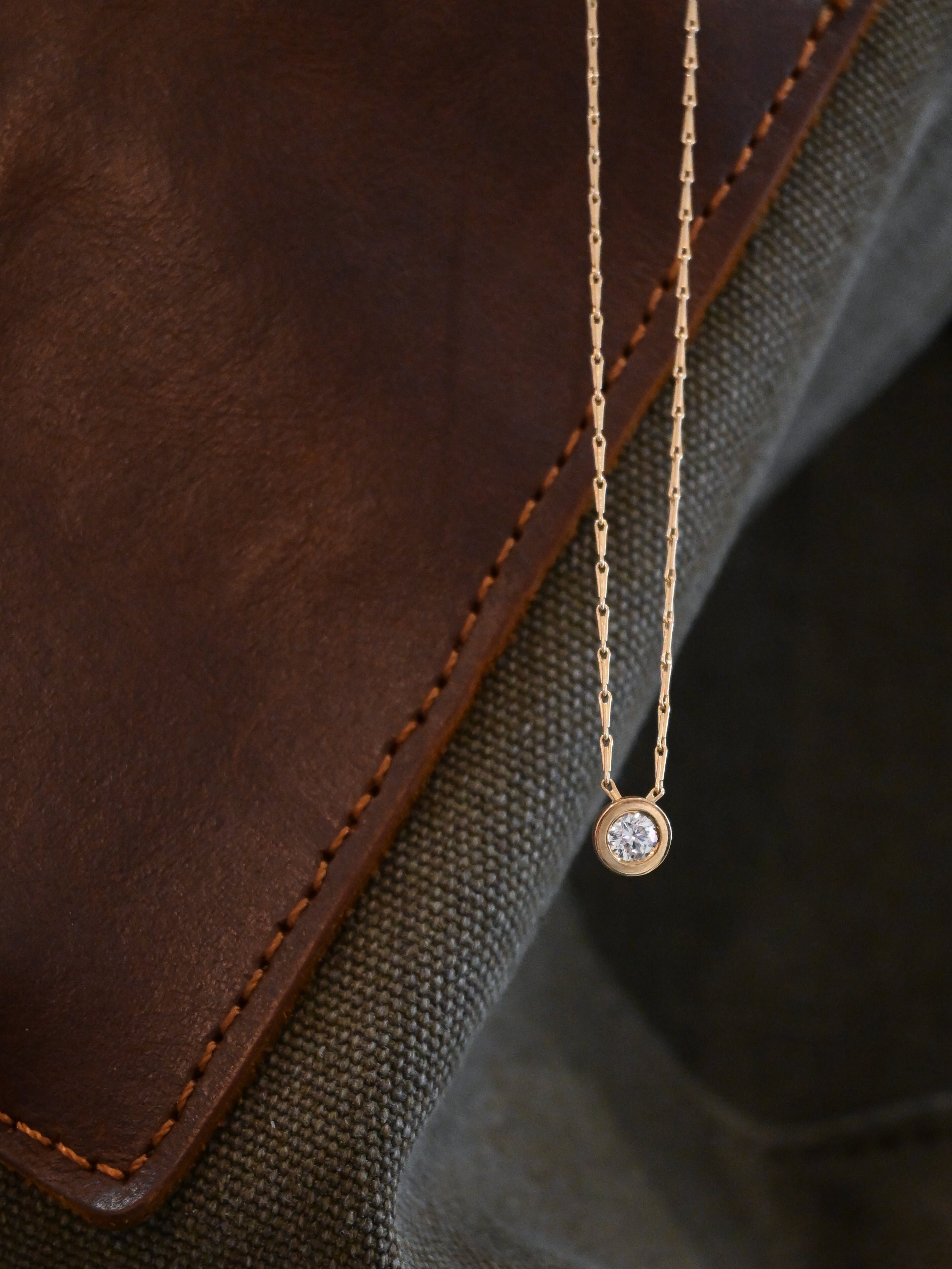 Gold necklace with a diamond pendant on a brown leather surface