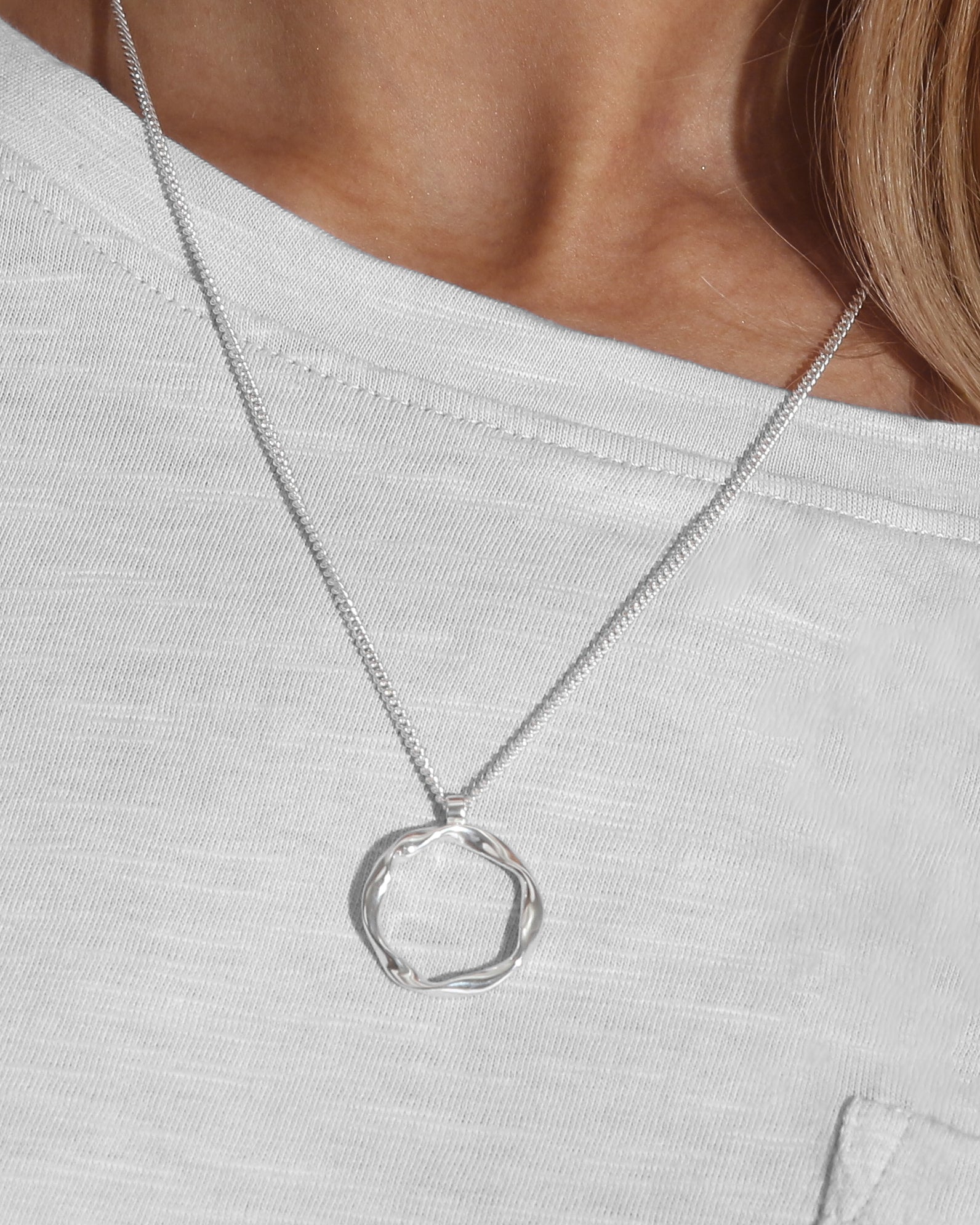 Alternative close up of model wearing a silver pendant necklace with a twisted circle design on an 18 inch curb chain